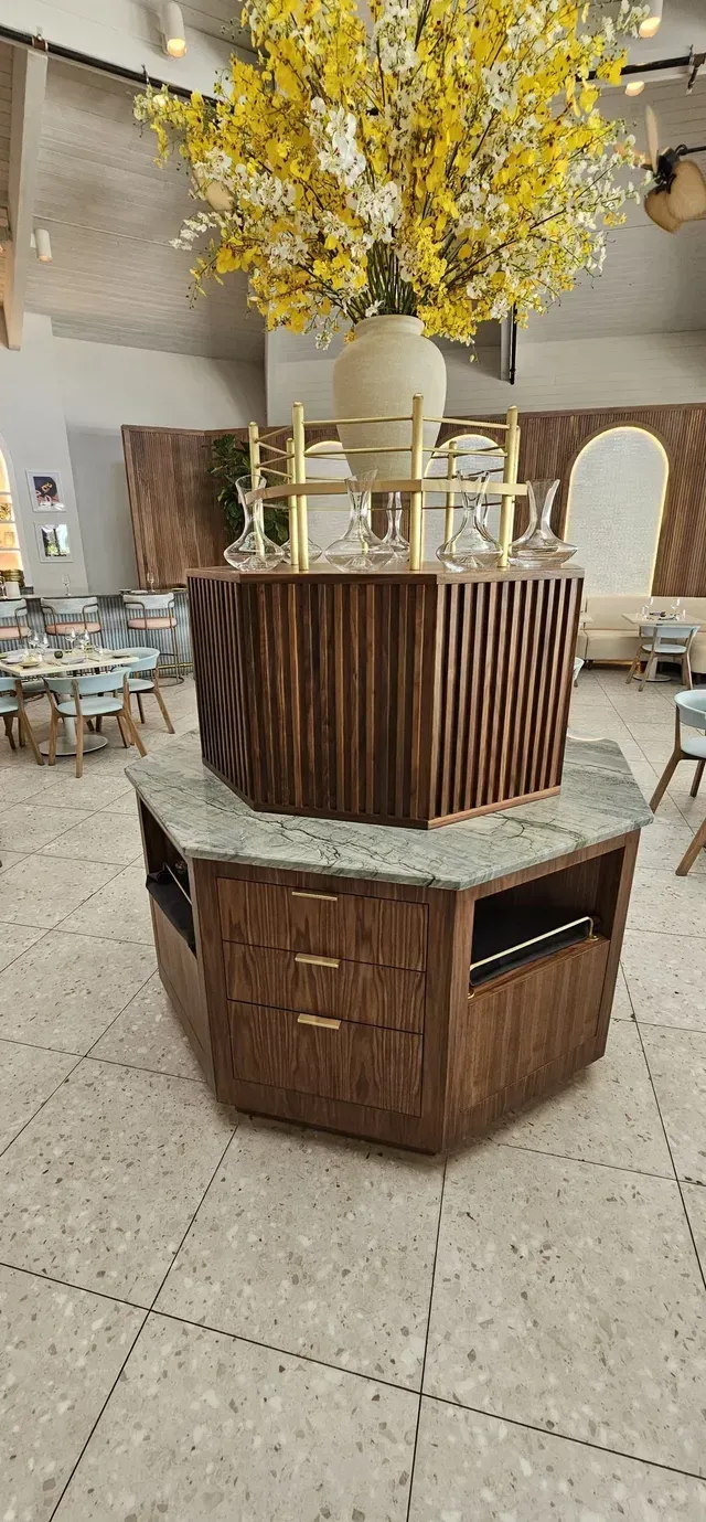 Decorative wooden display pedestal with yellow flowers in a store or lobby.