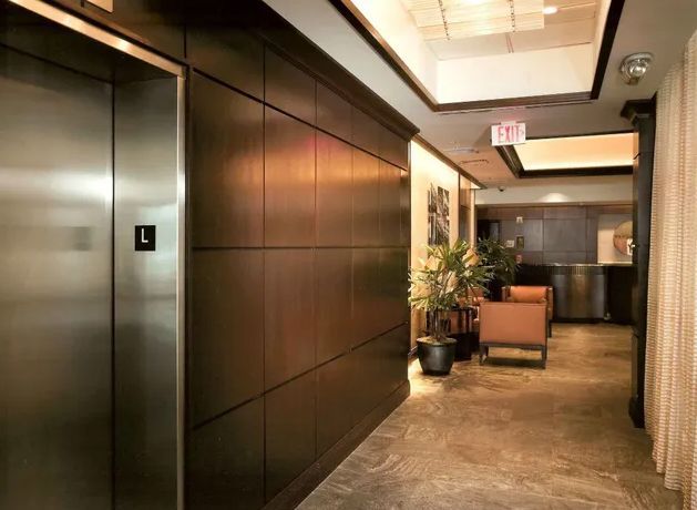 Office hallway with elevator, wood-paneled walls, and potted plants.