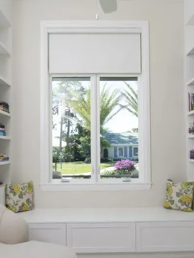 White window seat nook with built-in drawers, floral cushions, and a view of a sunny palm-lined yard.