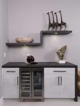 Modern cabinet with glass wine cooler, dark countertop, and two floating shelves with decorative items.