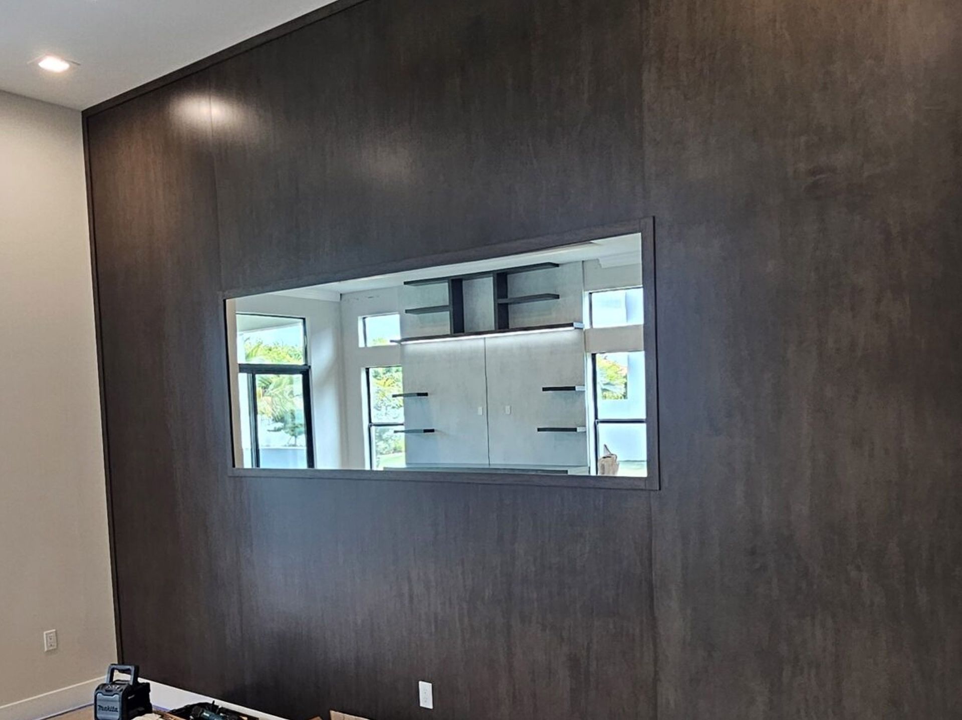 Dark wood accent wall with a rectangular pass-through window into a bright kitchen.