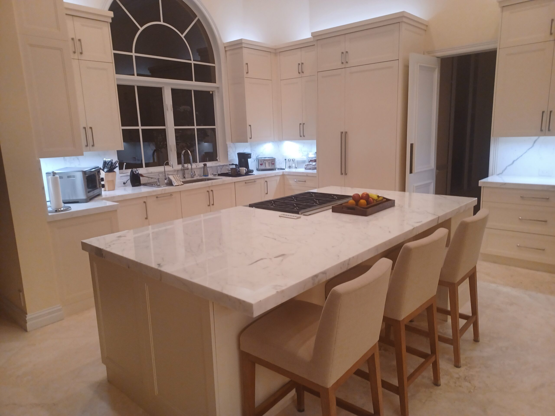 Bright modern kitchen with a large marble island, four stools, and a window over the sink
