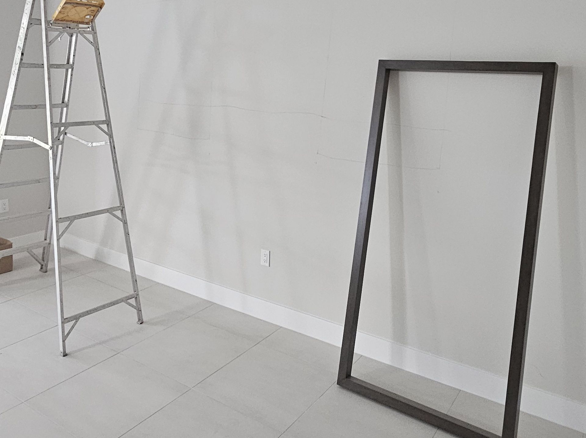 Empty room with a step ladder and a black-framed mirror leaning against the wall.