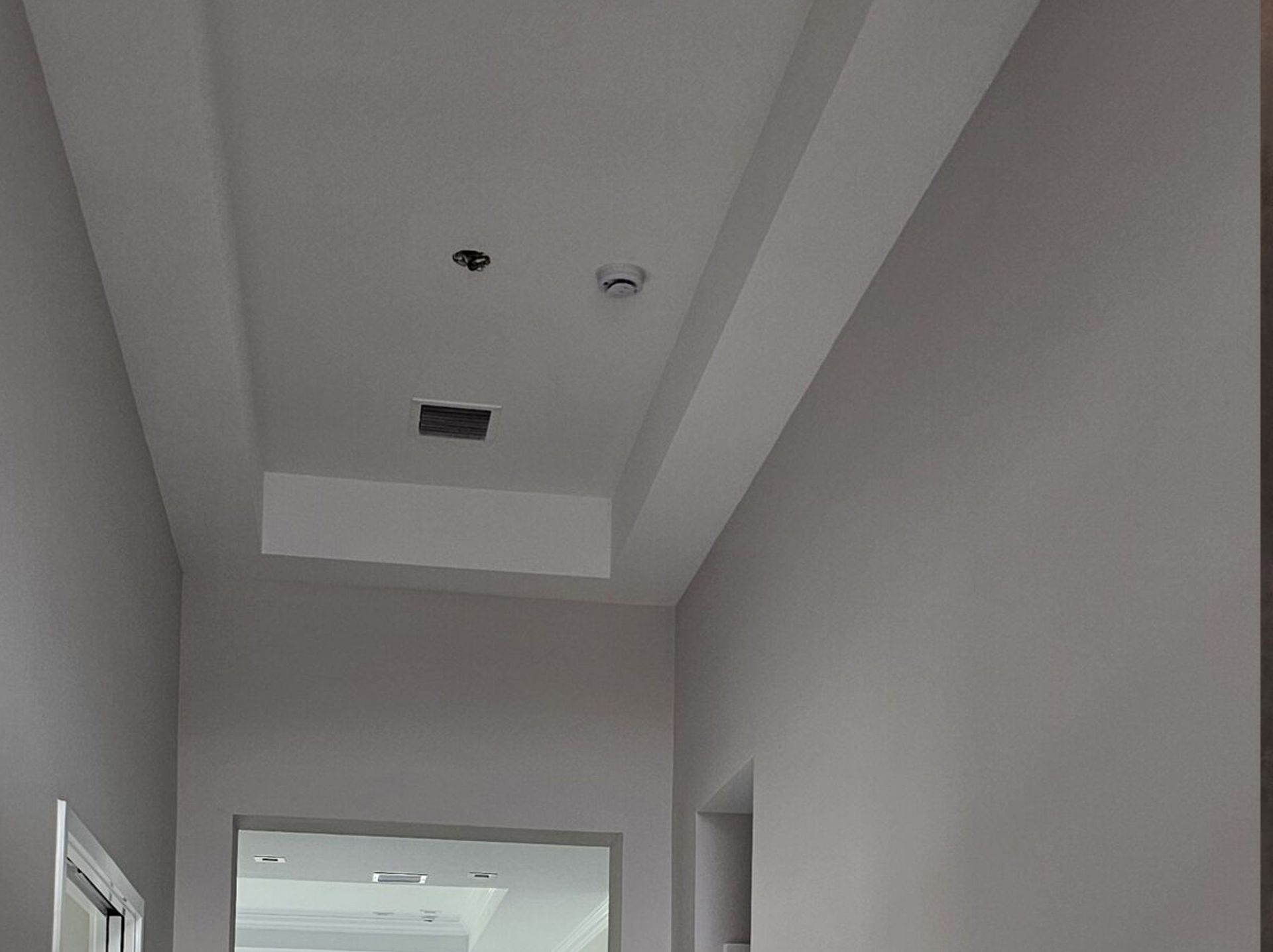 Hallway ceiling with recessed light fixtures and a vent, above a doorway.