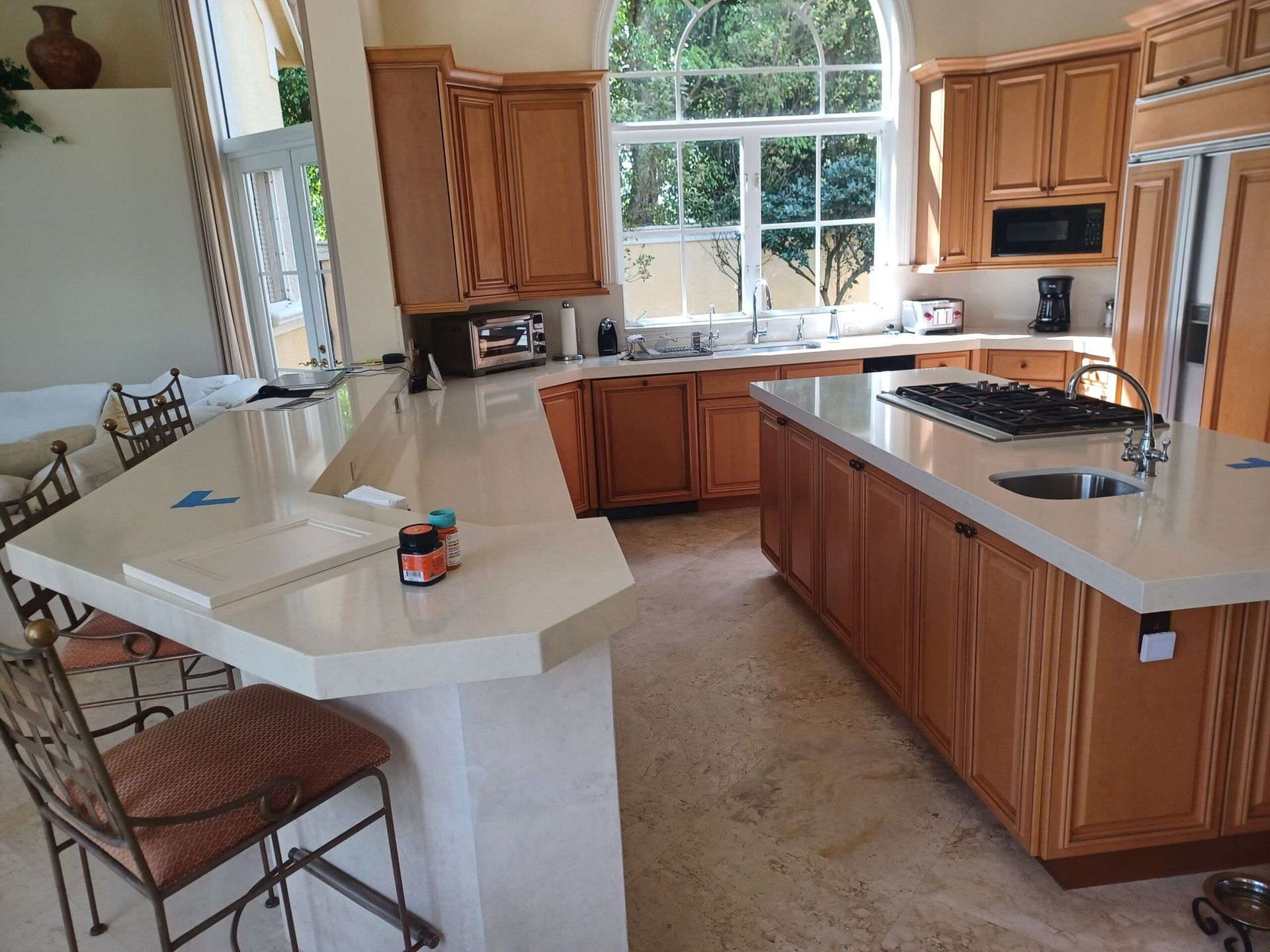Bright kitchen with wood cabinets, white countertops, island seating, and a large window