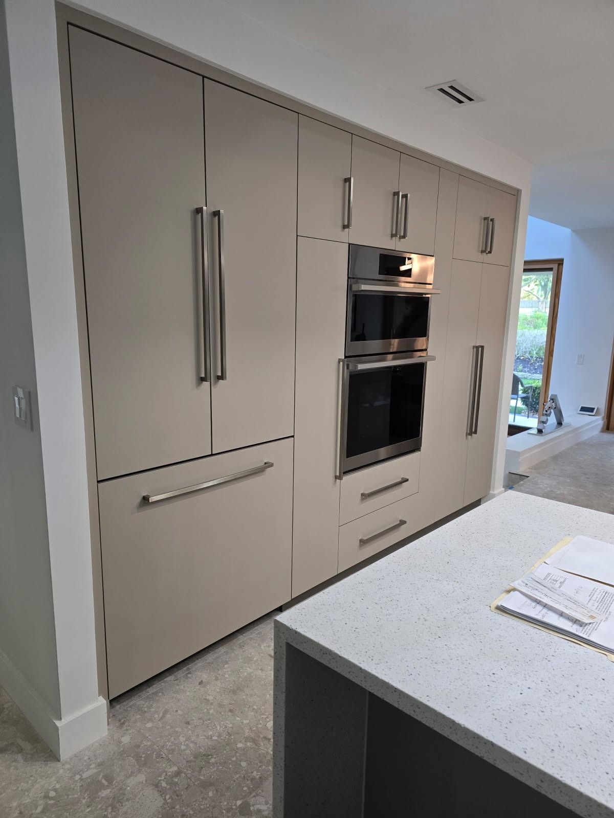 Built-in beige kitchen wall with double ovens and tall cabinets beside a light countertop