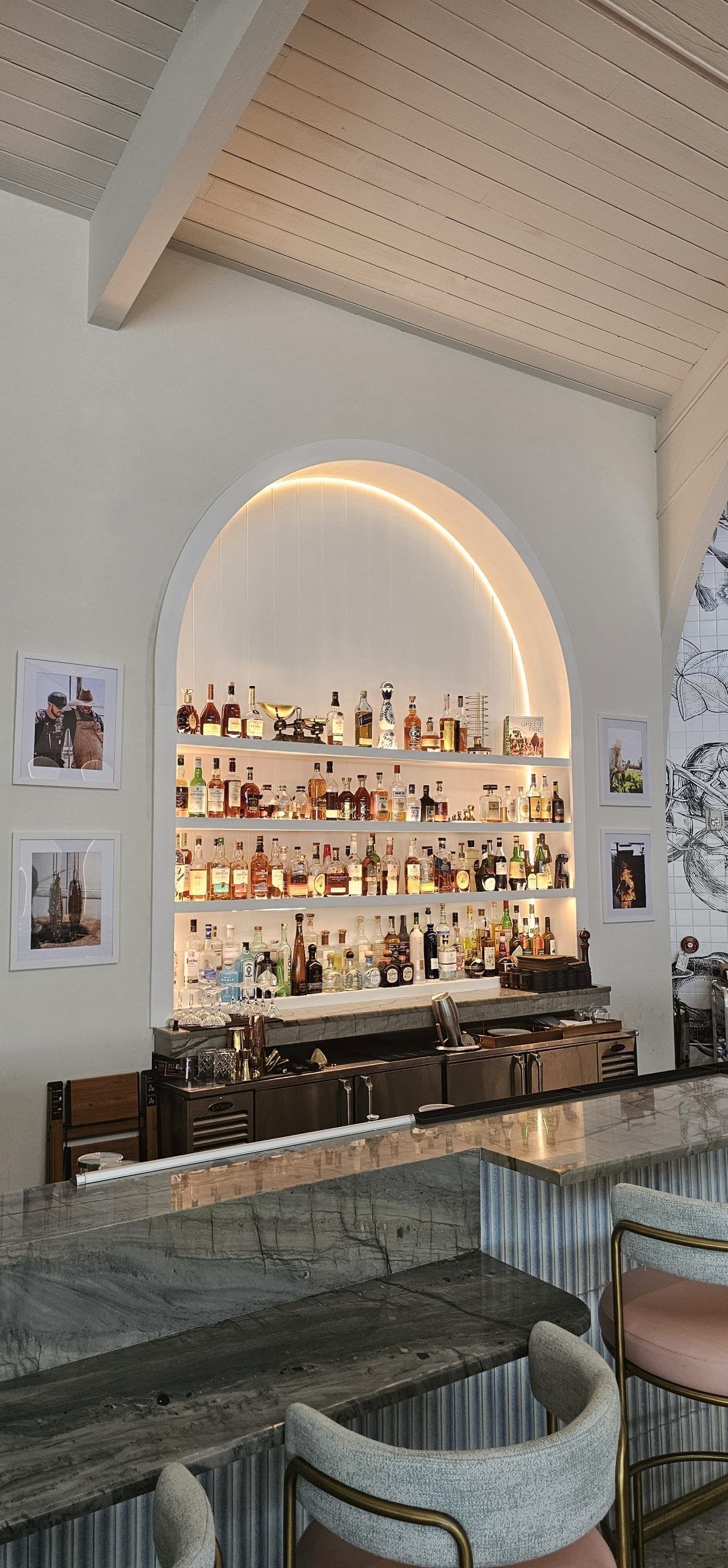 Stylish bar with arched backlit shelves, glassware, and cushioned seating under a vaulted ceiling.