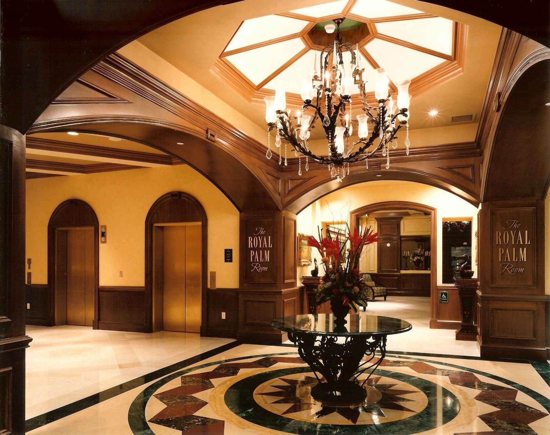 Elegant hotel lobby with ornate wood arches, chandelier, and circular floral floor design.