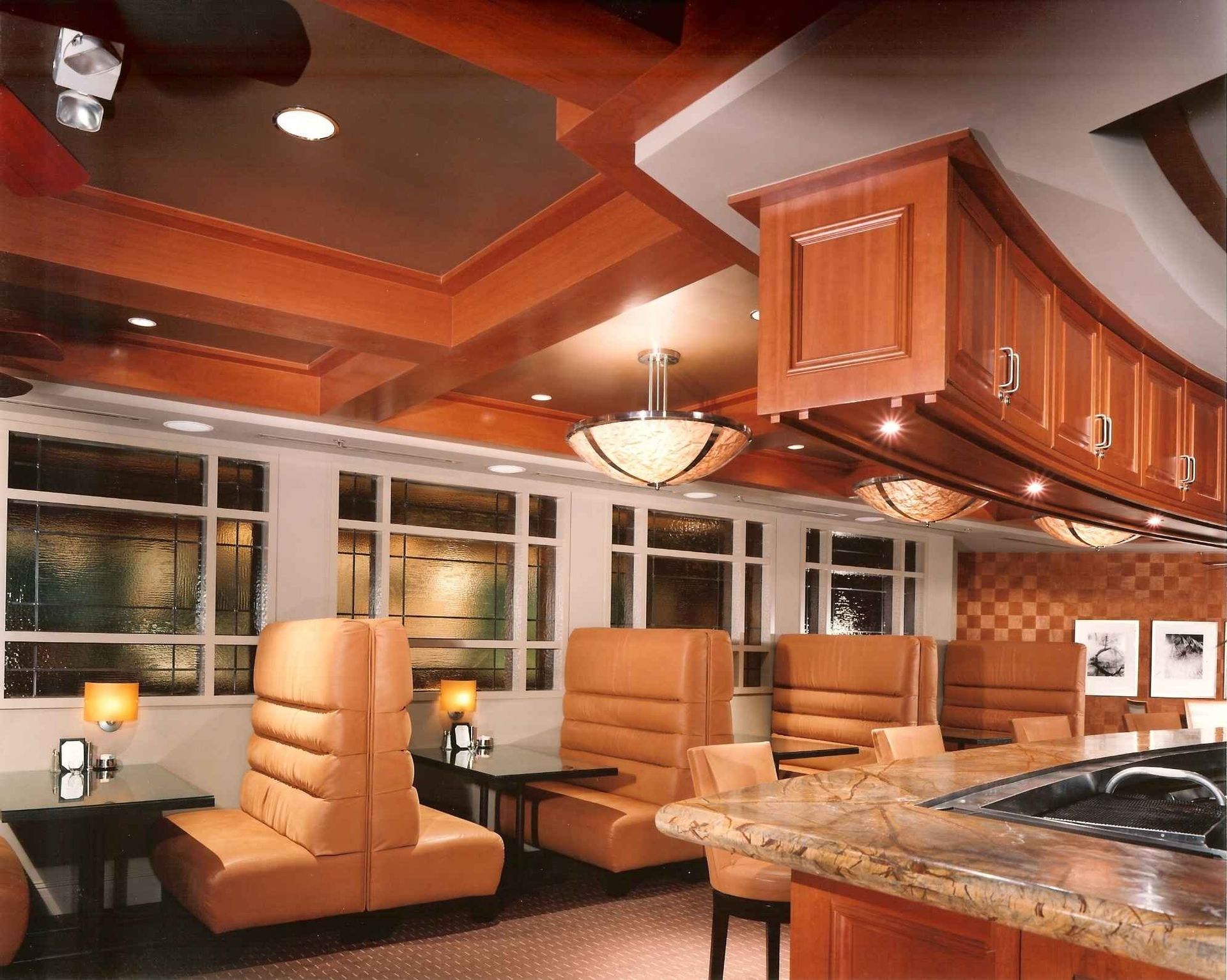 Warm kitchen with wood cabinetry, tan leather chairs, granite island, and recessed ceiling lighting