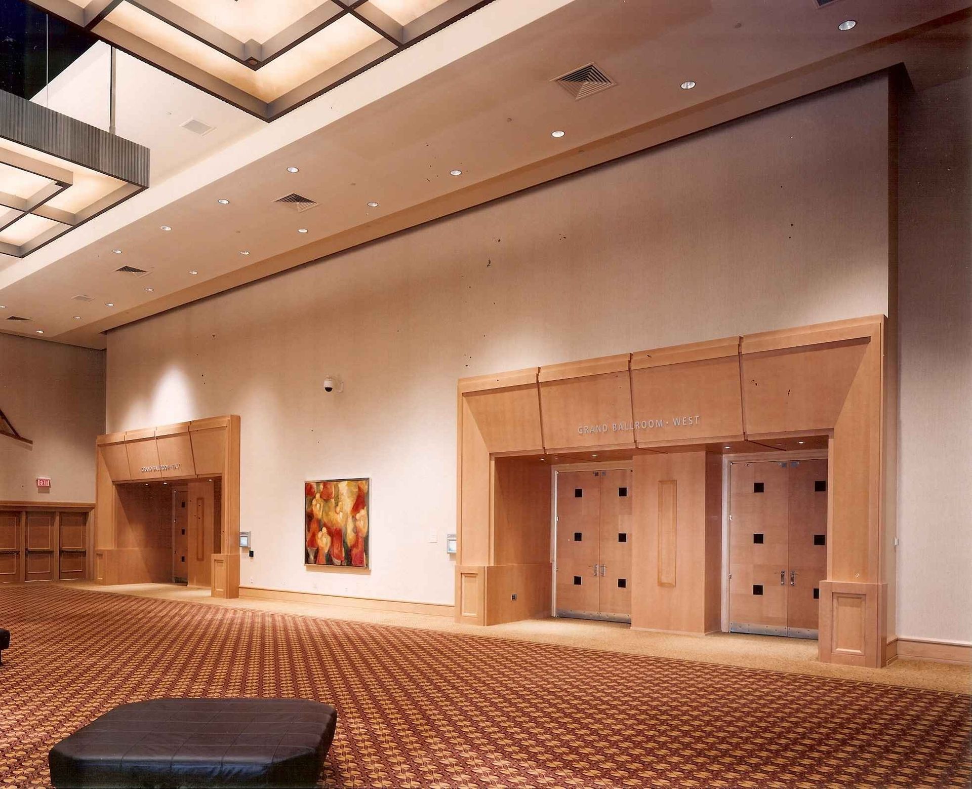 Empty hotel lobby with patterned carpet, wood-paneled elevator doors, and high ceiling lights