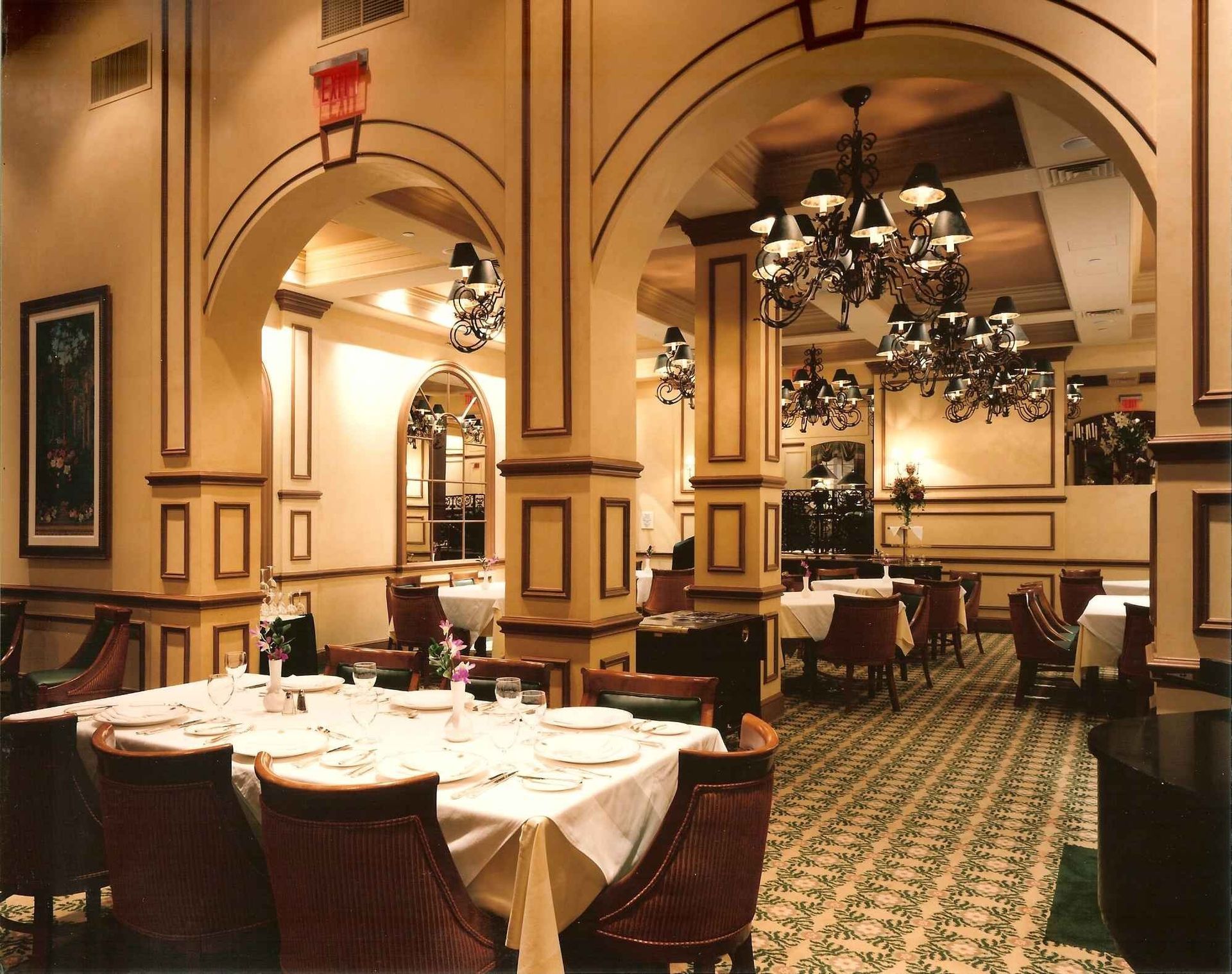 Elegant restaurant dining room with arched ceilings, chandeliers, and white-tablecloth tables on patterned carpet