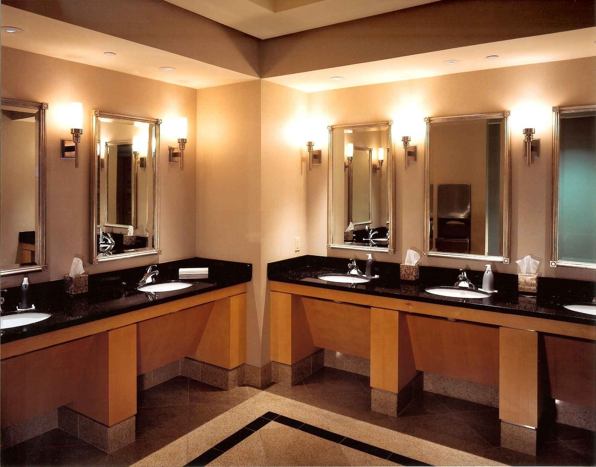 Public restroom with beige walls, black countertops, and three lit mirrors above sinks
