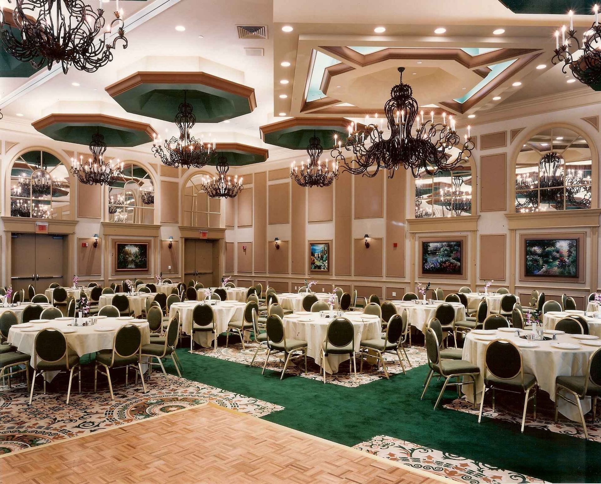 Elegant banquet hall with round tables, green carpet runners, chandeliers, and ornate ceiling decor