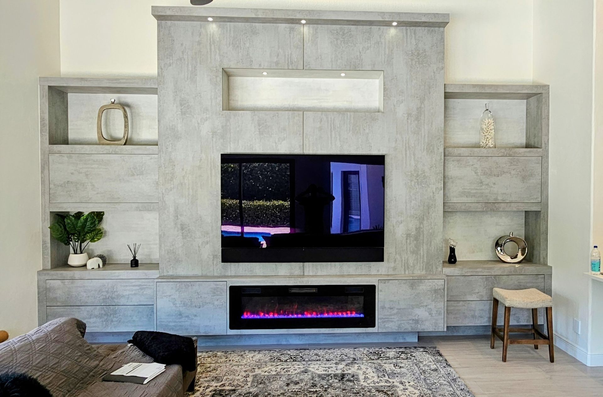 Modern living room with built-in gray shelving, wall-mounted TV, and electric fireplace beneath a large white mantel