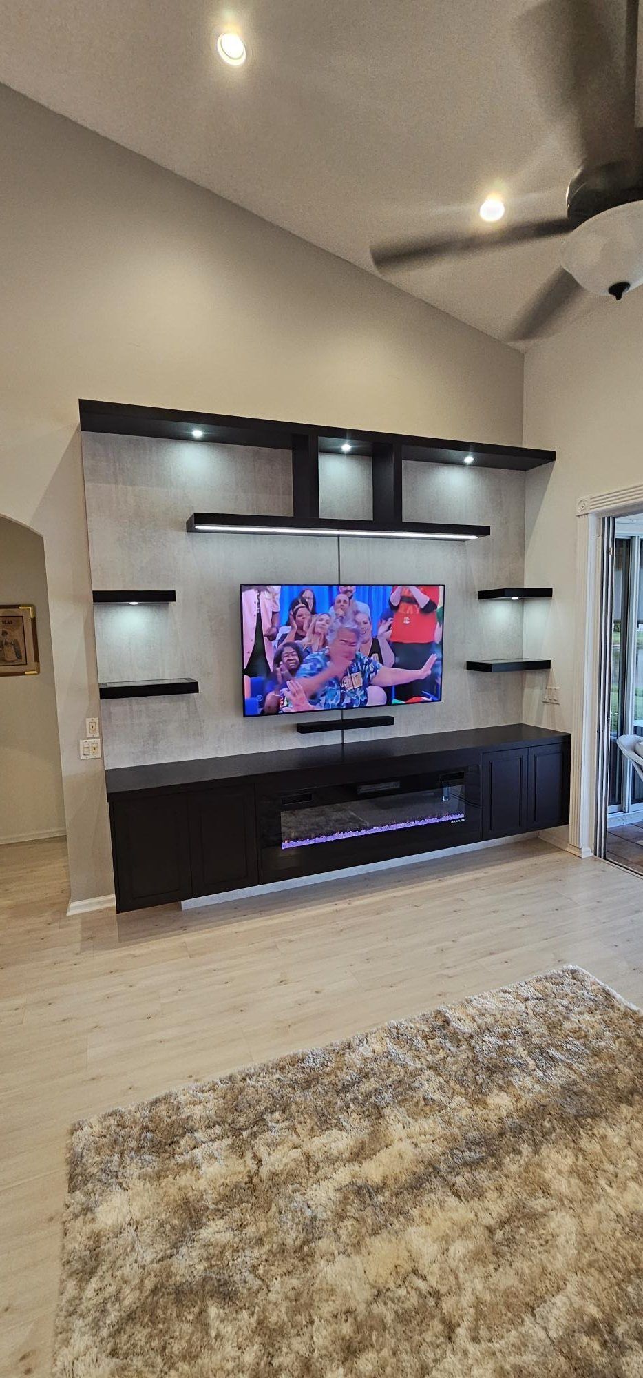 Modern living room with wall-mounted TV on a dark entertainment unit and a patterned rug on light tile flooring