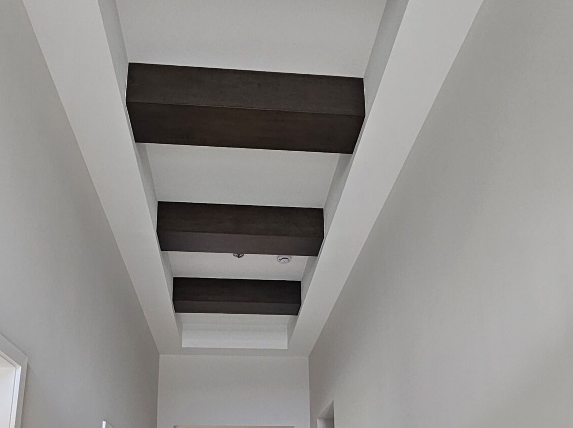 White hallway ceiling with exposed dark wooden beams above.