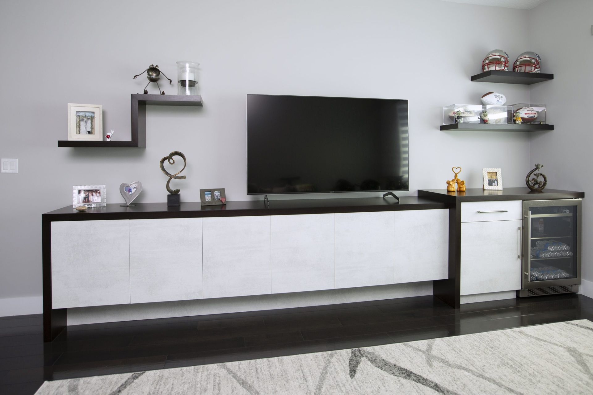 Modern living room with TV, white media console, wall shelves, and small glass cabinet