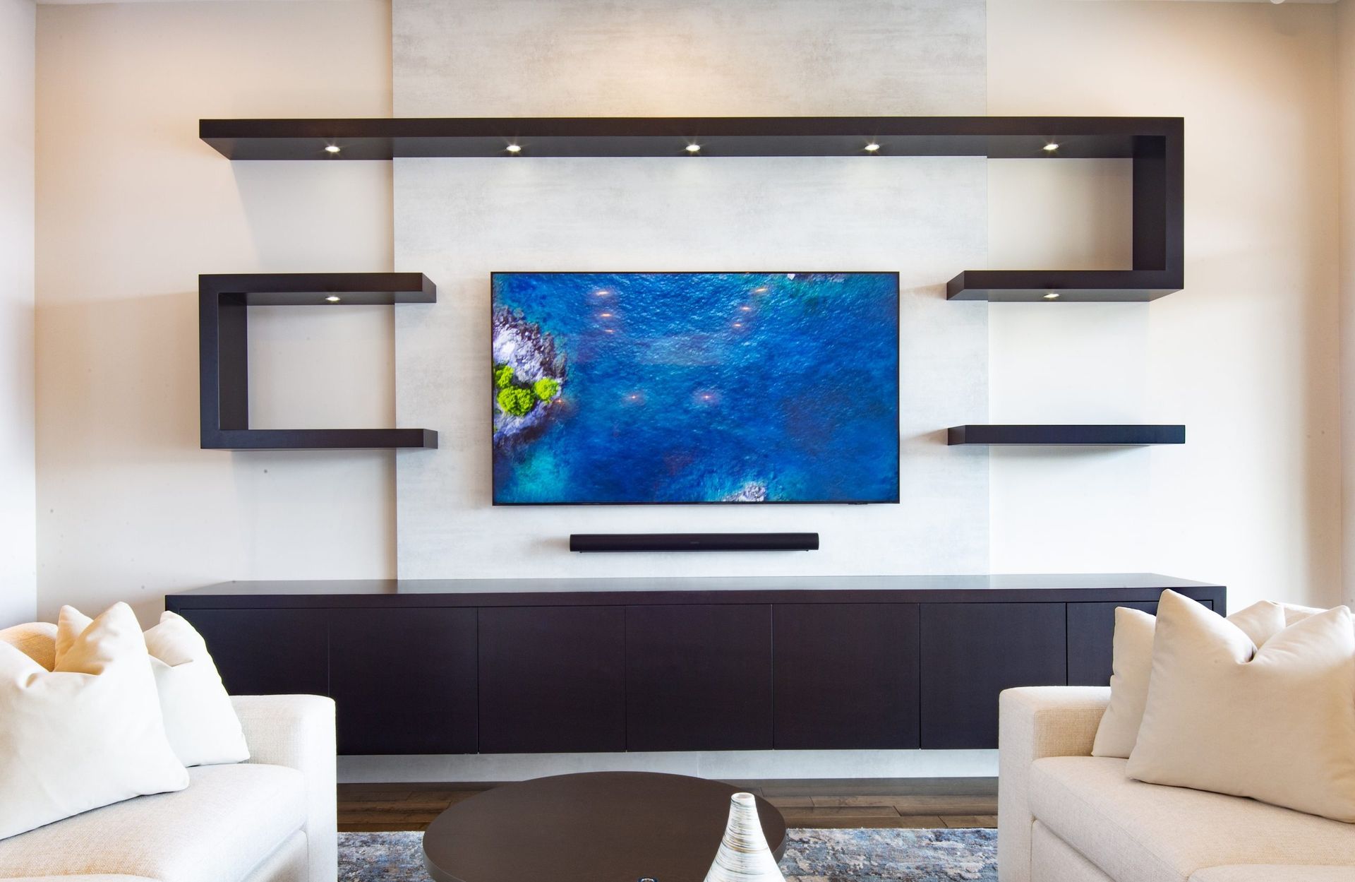 Modern living room with wall-mounted TV, floating shelves, and beige sofas