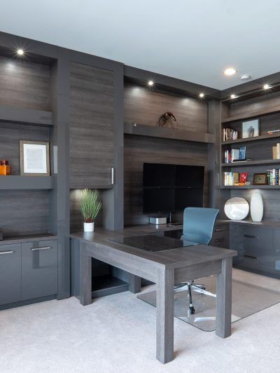 Modern home office with built-in dark wood shelves, desk, TV, and a blue chair
