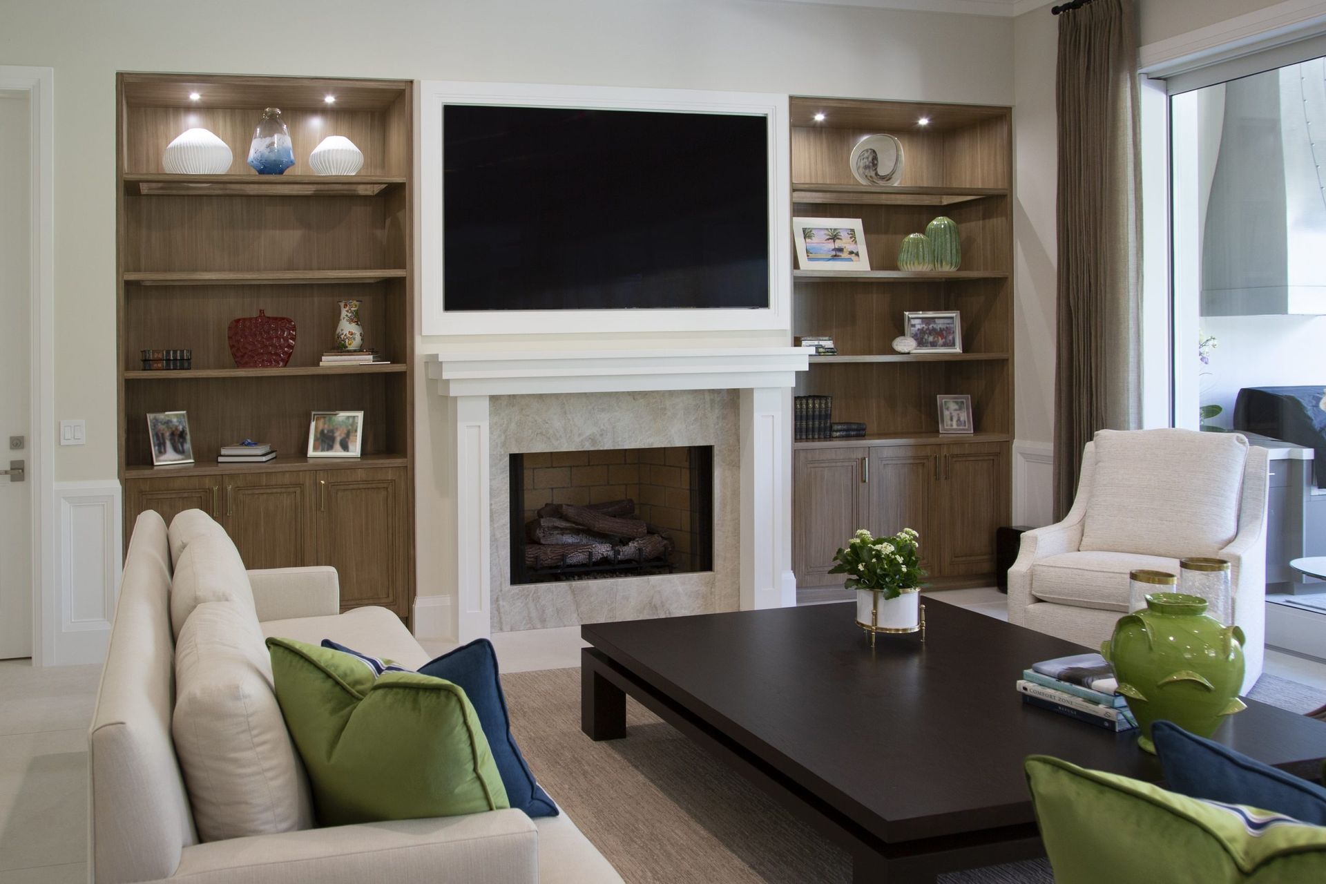 Bright living room with fireplace, TV, built-in shelves, white sofas, and a dark coffee table