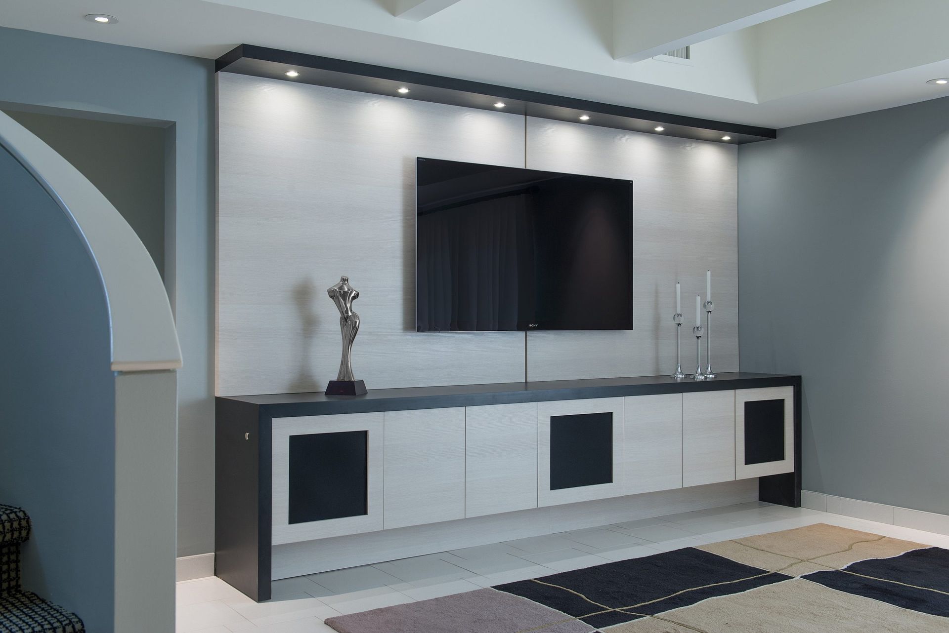 Modern living room with wall-mounted TV, white console, gray walls, and patterned rug