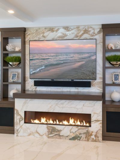 Modern living room with marble fireplace, wall-mounted TV, and built-in shelves displaying decor