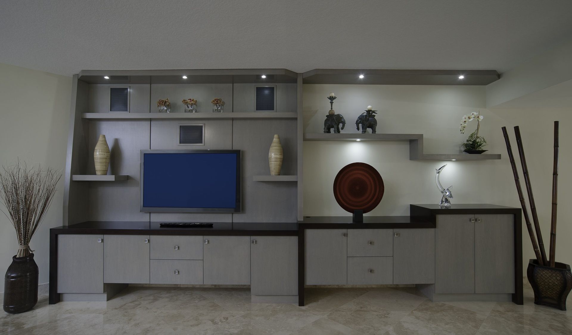 Modern living room TV wall unit in beige and gray with shelves, cabinets, and decorative vases