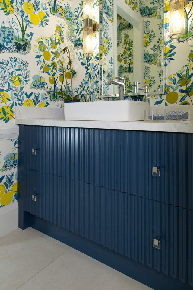 Blue vanity with white sink and floral wallpaper in a bright bathroom.