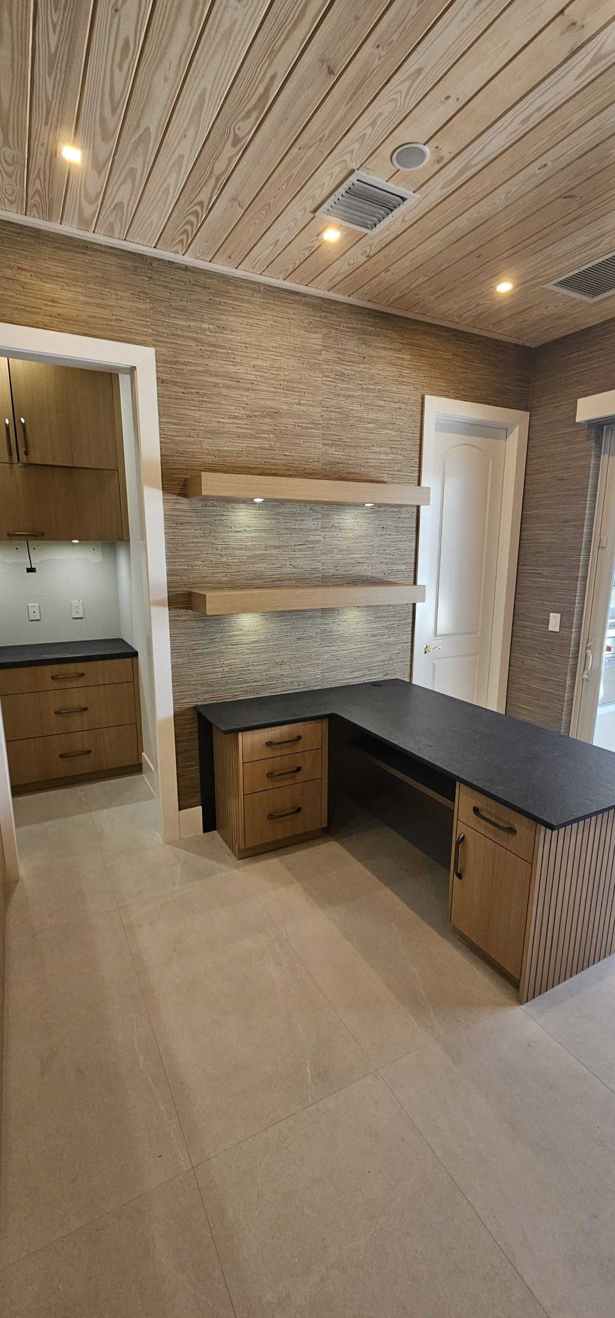 Stone-walled room with wood ceiling, black worktable, small desk, shelves, and white door.