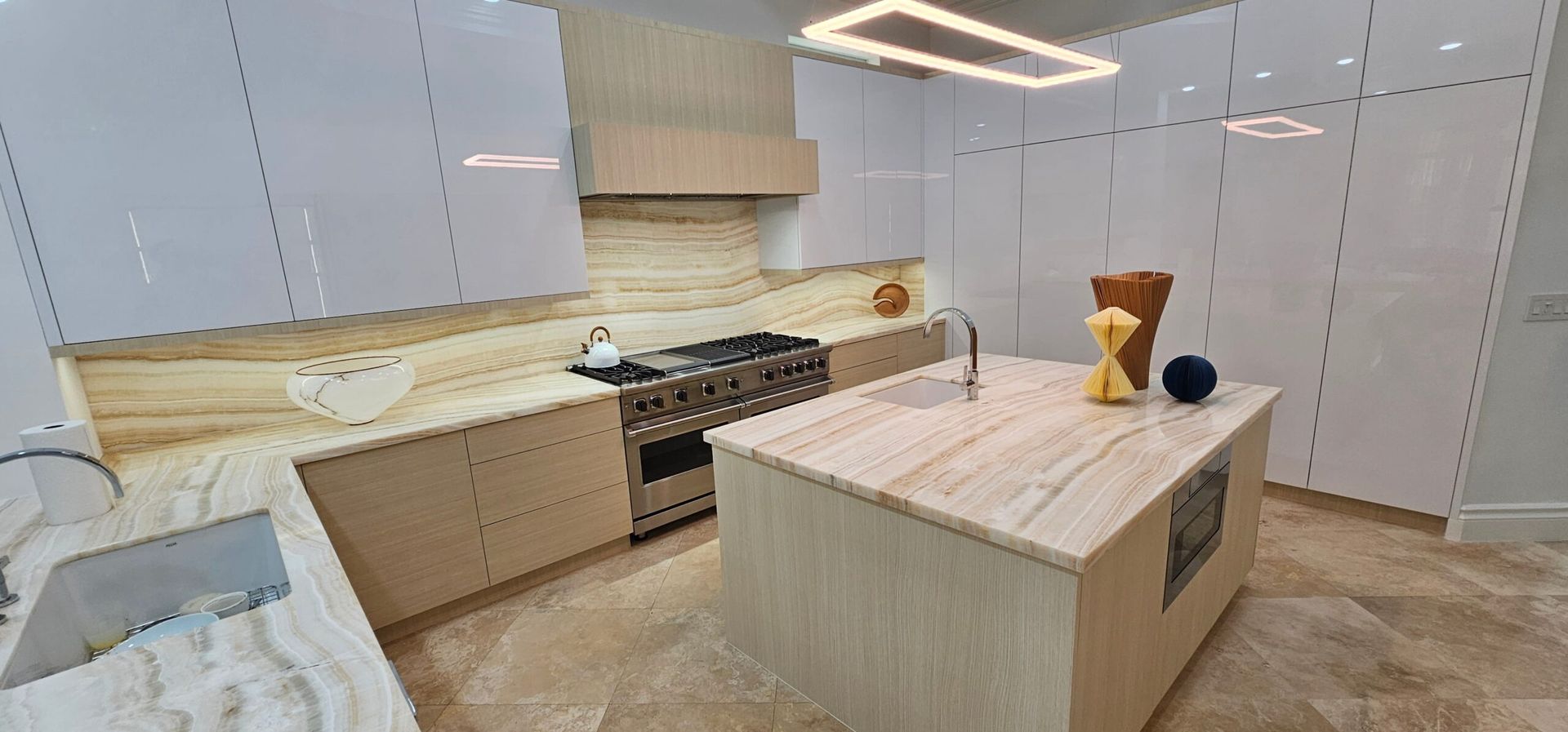 Modern white kitchen with island, marble countertops, and stainless-steel stove under a geometric ceiling light
