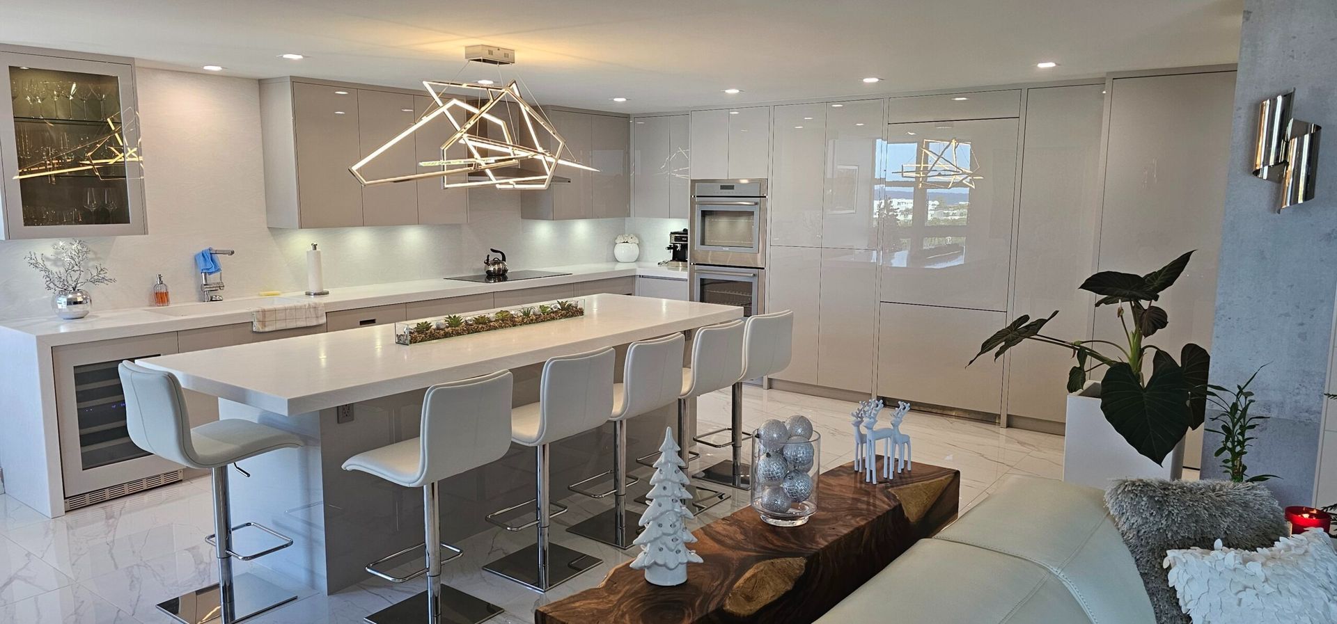 Bright modern kitchen and dining area with white cabinets, island stools, and a wooden coffee table in the foreground