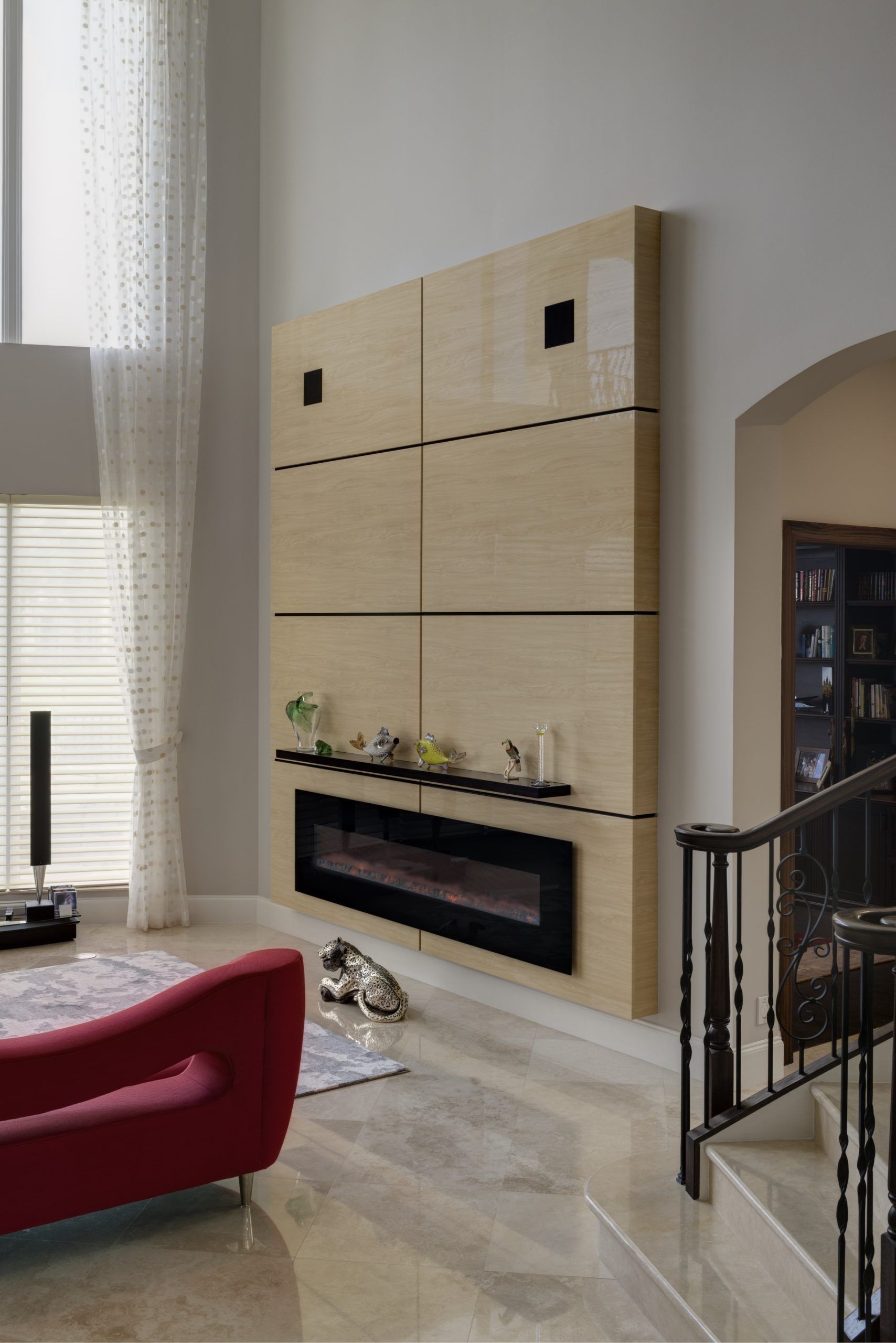 Modern living room with a beige tiled fireplace, red chair, and staircase railing