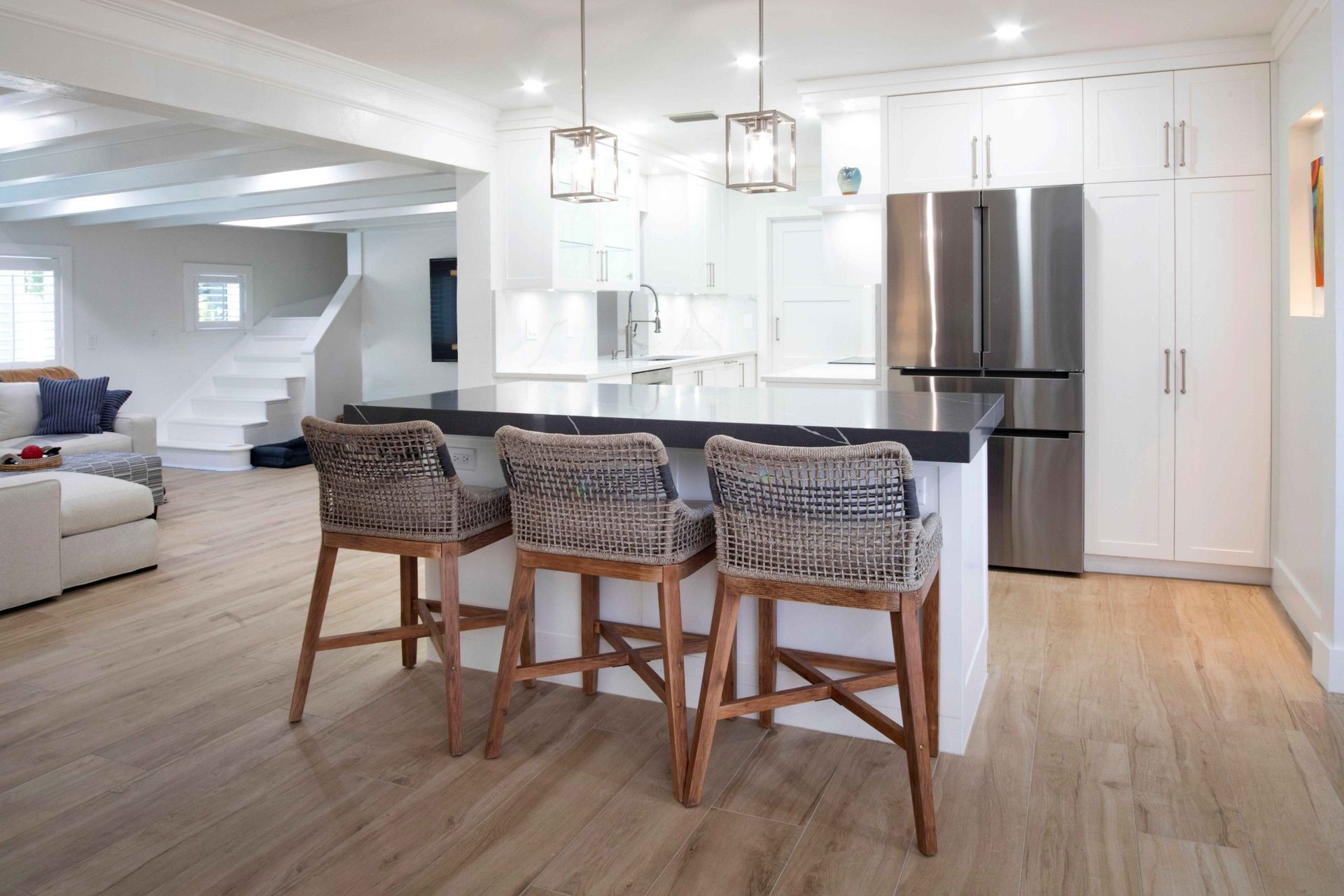 Bright open kitchen with island, three woven stools, stainless fridge, and light wood floors