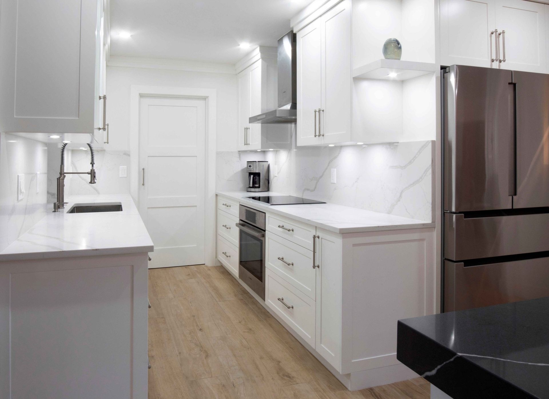 Modern white galley kitchen with stainless steel appliances, wood floor, and marble-look countertops