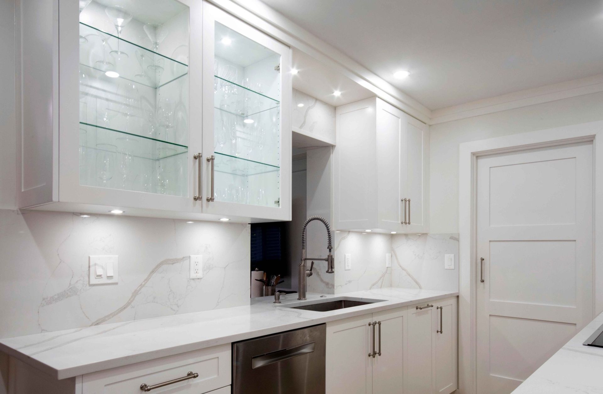 Bright white modern kitchen with glass cabinets, marble countertops, and stainless steel appliances