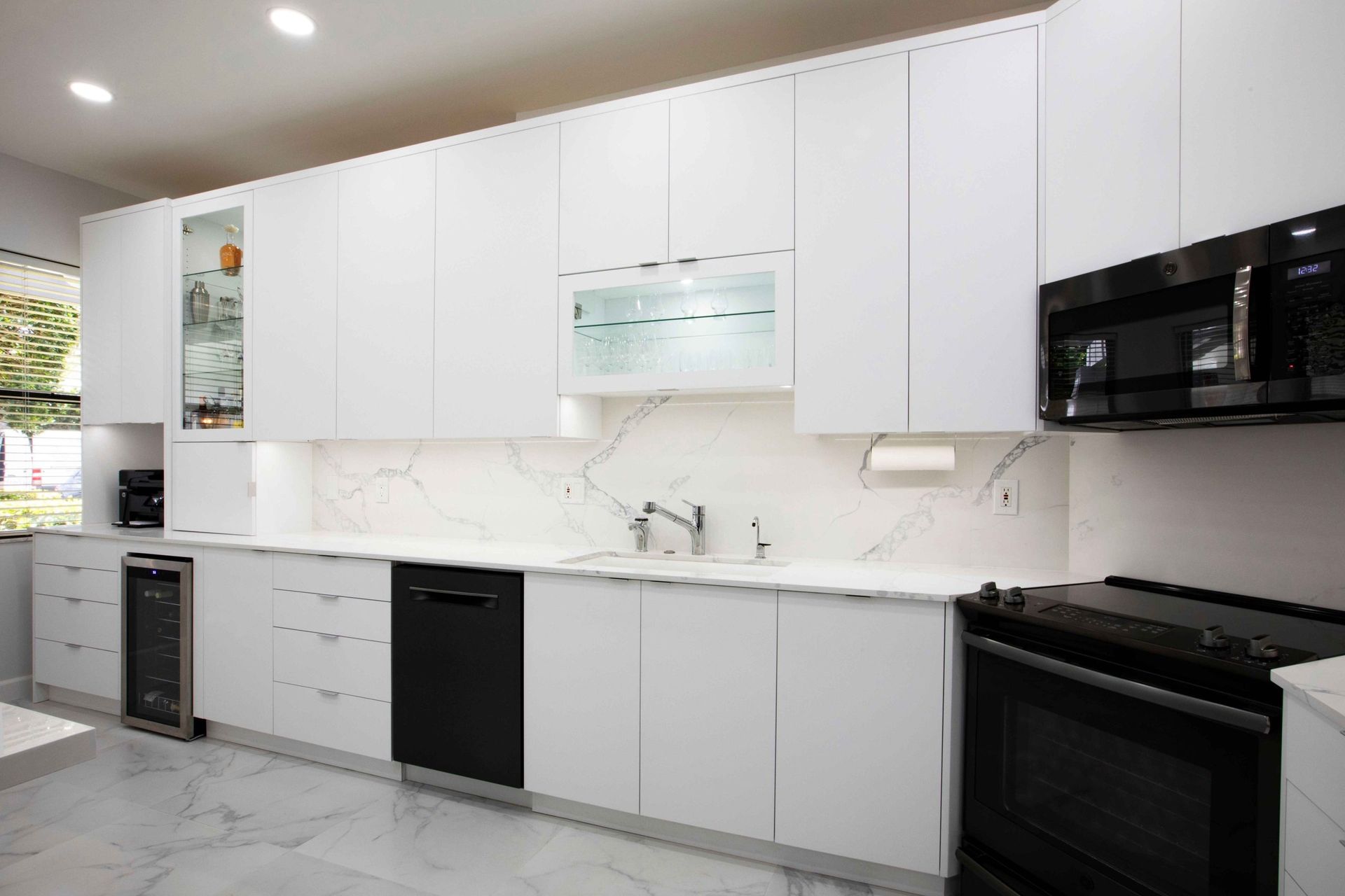 Modern white kitchen with black appliances, marble backsplash, and light gray floor cabinets