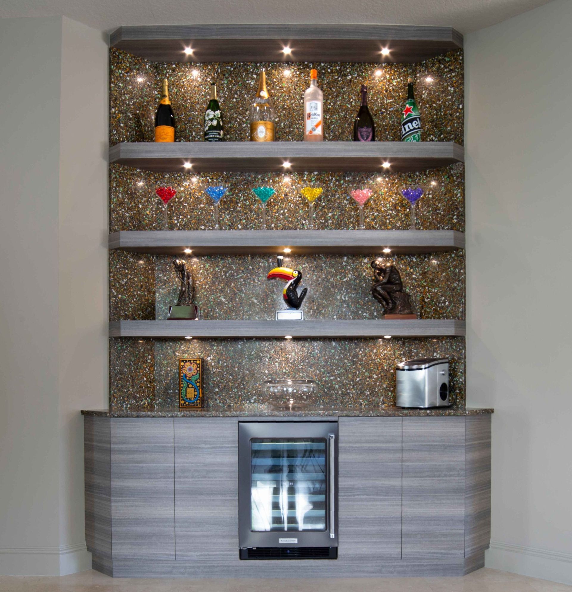 Home bar with mirrored shelves, colorful glassware, liquor bottles, and a wine cooler below