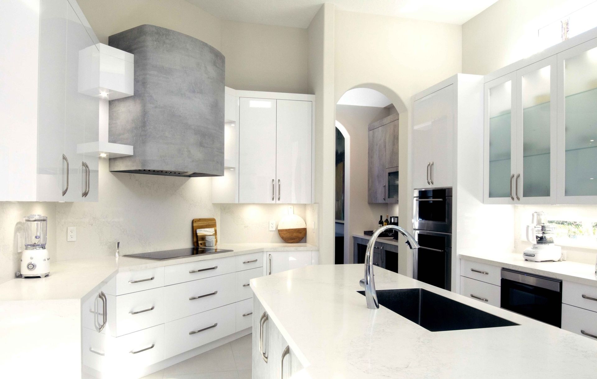 Bright modern white kitchen with island, stainless appliances, and arched doorway