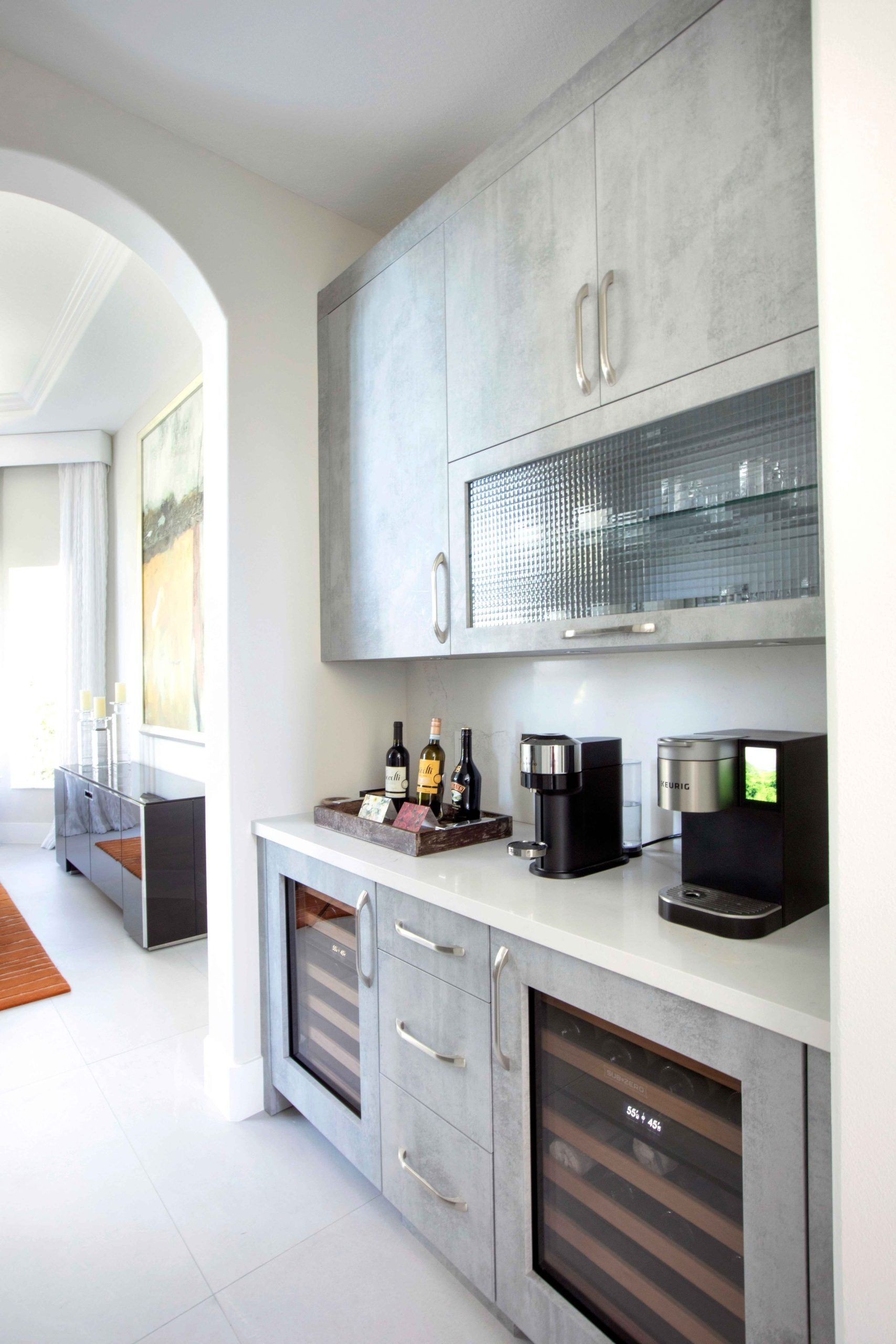 Bright modern kitchen alcove with white cabinets, black countertop, and wine fridge under arched doorway