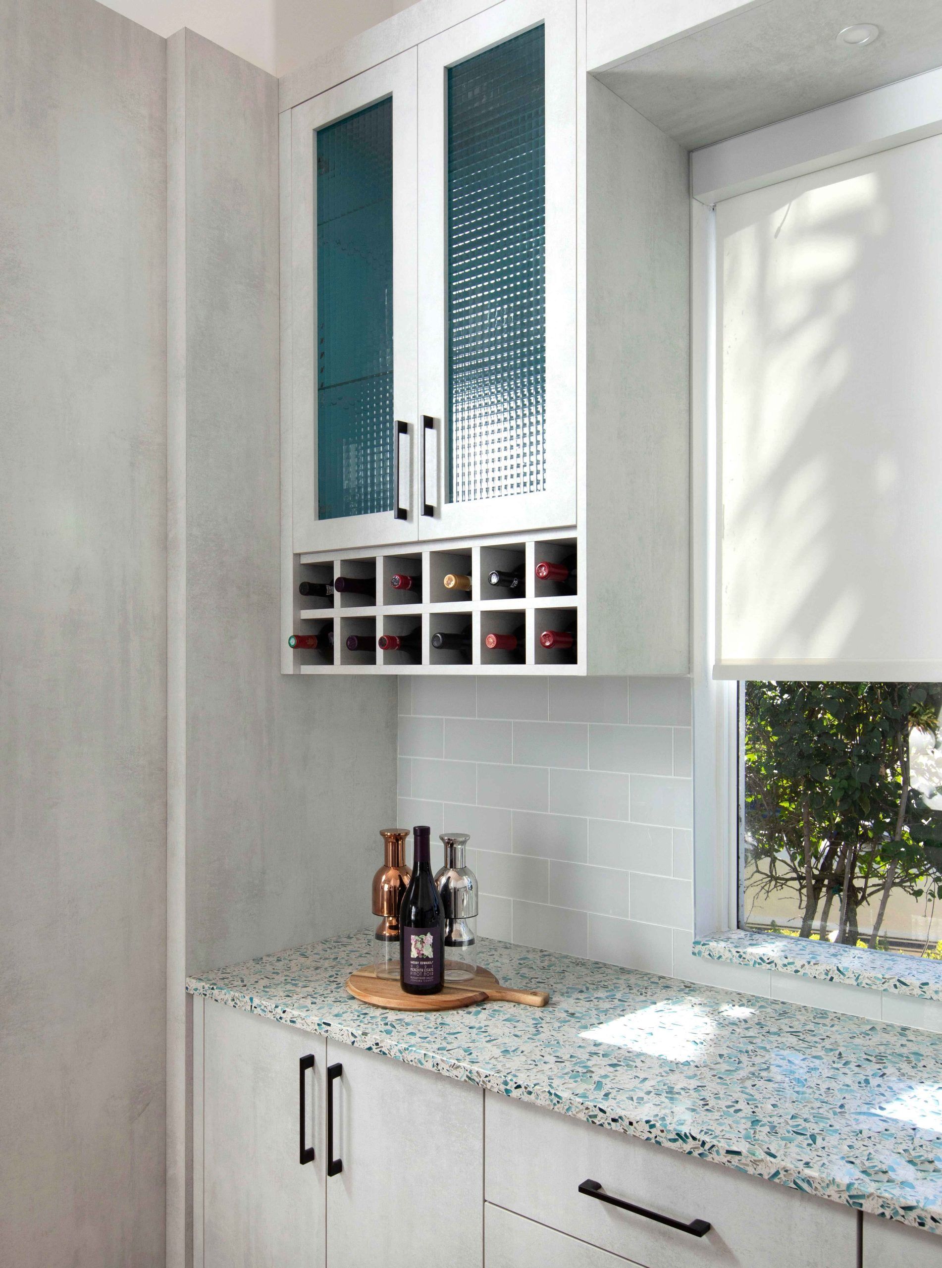 Bright kitchen corner with white cabinets, speckled countertop, spice rack, and window light.