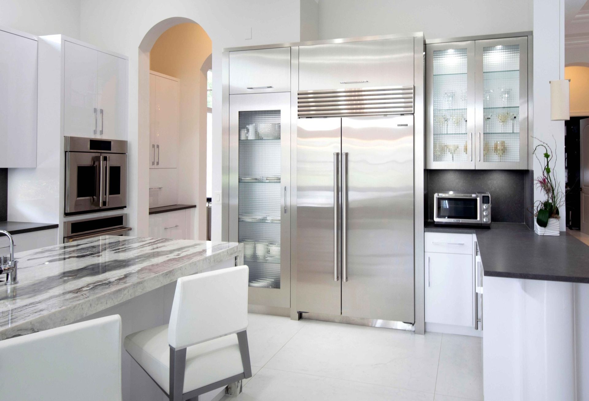 Modern white kitchen with stainless steel appliances, island, and glass-front refrigerator