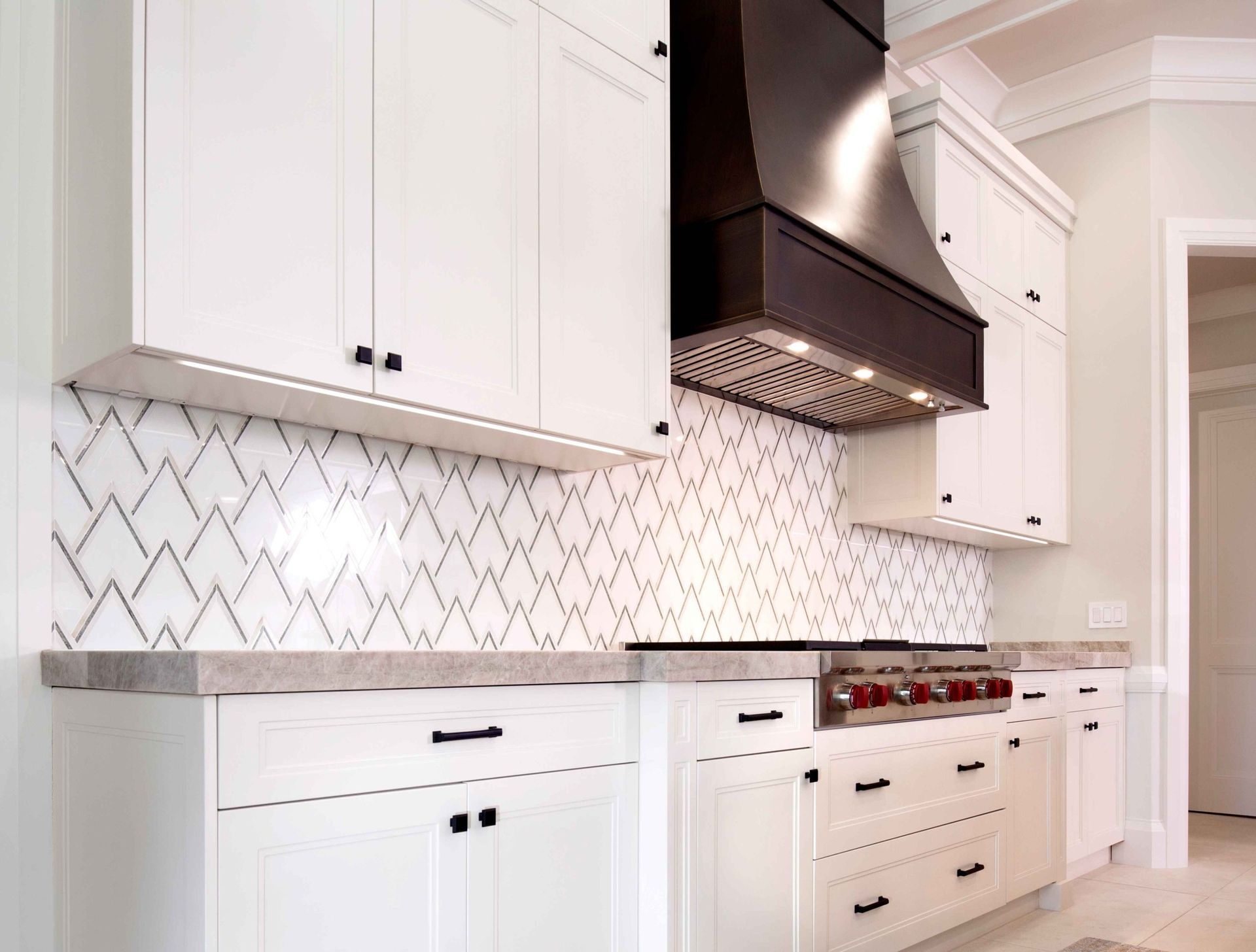 Bright white kitchen with patterned backsplash, black range hood, and built-in cabinets