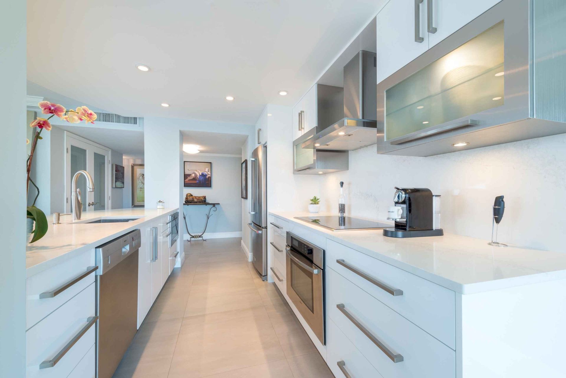 Bright modern kitchen with white cabinets, stainless appliances, and a long central walkway