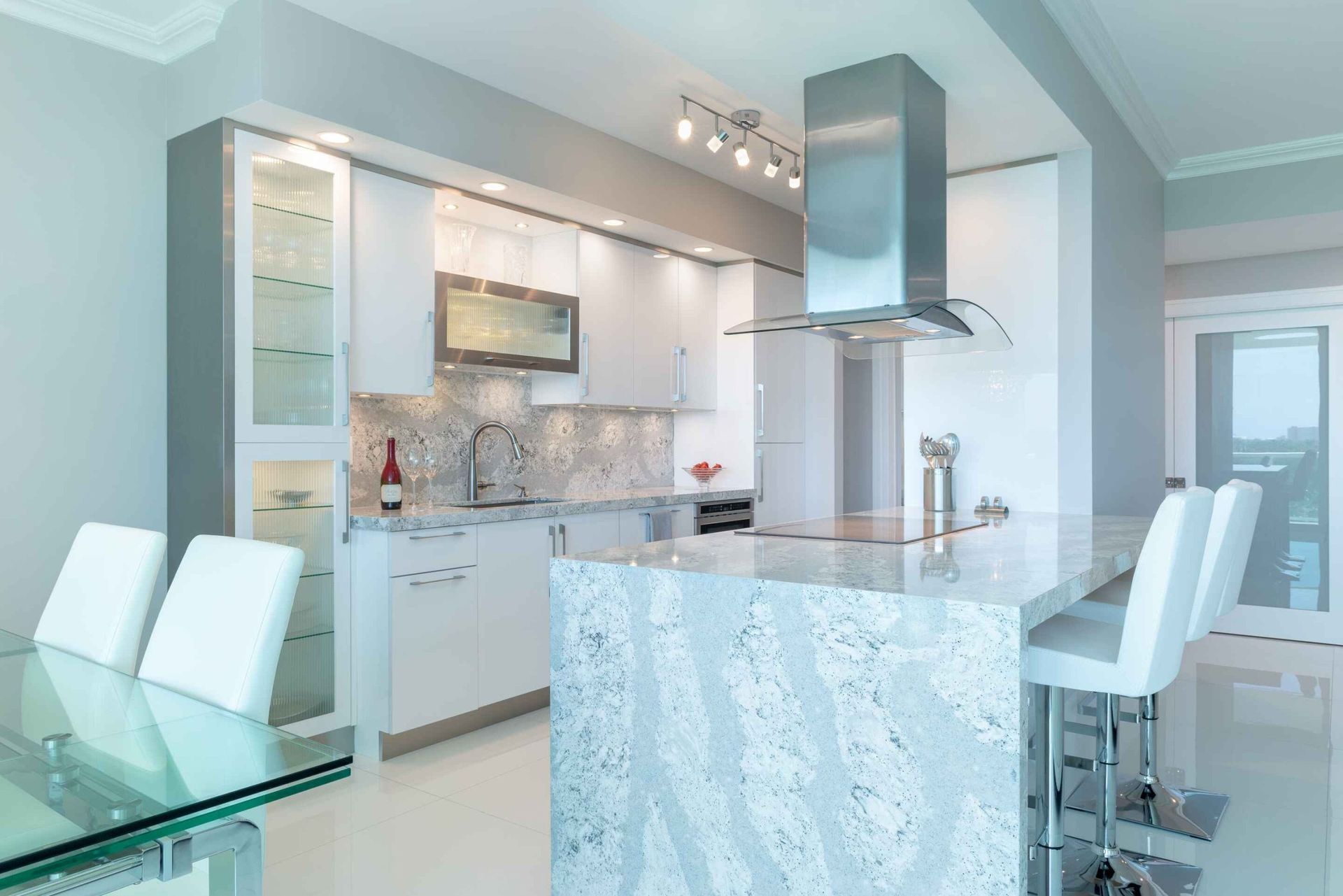 Bright modern white kitchen with marble island, bar stools, and glass dining table