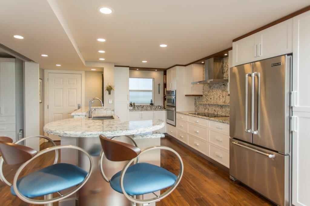 Bright modern kitchen with white cabinets, marble island, stainless steel appliances, and blue chairs