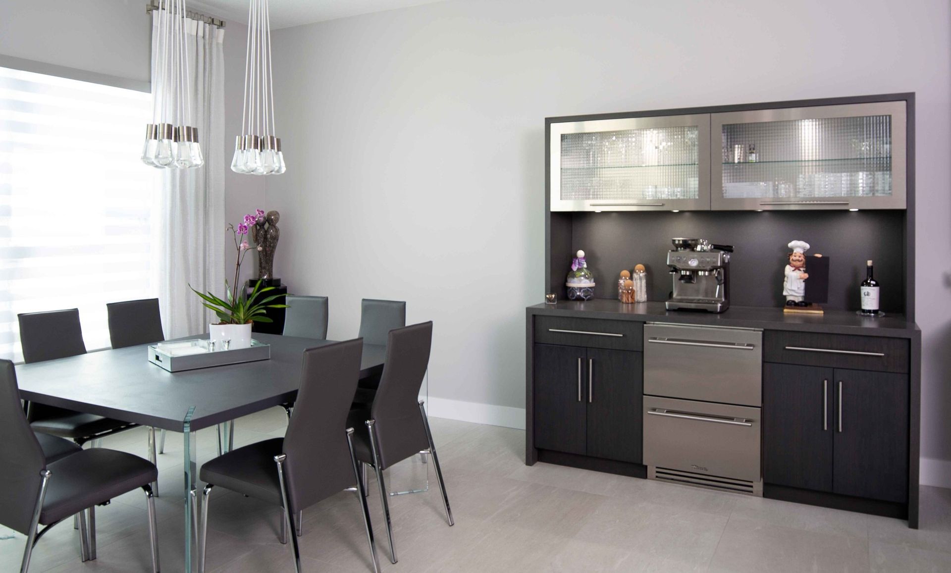 Modern dining room with gray table and chairs beside a black sideboard and glass cabinets