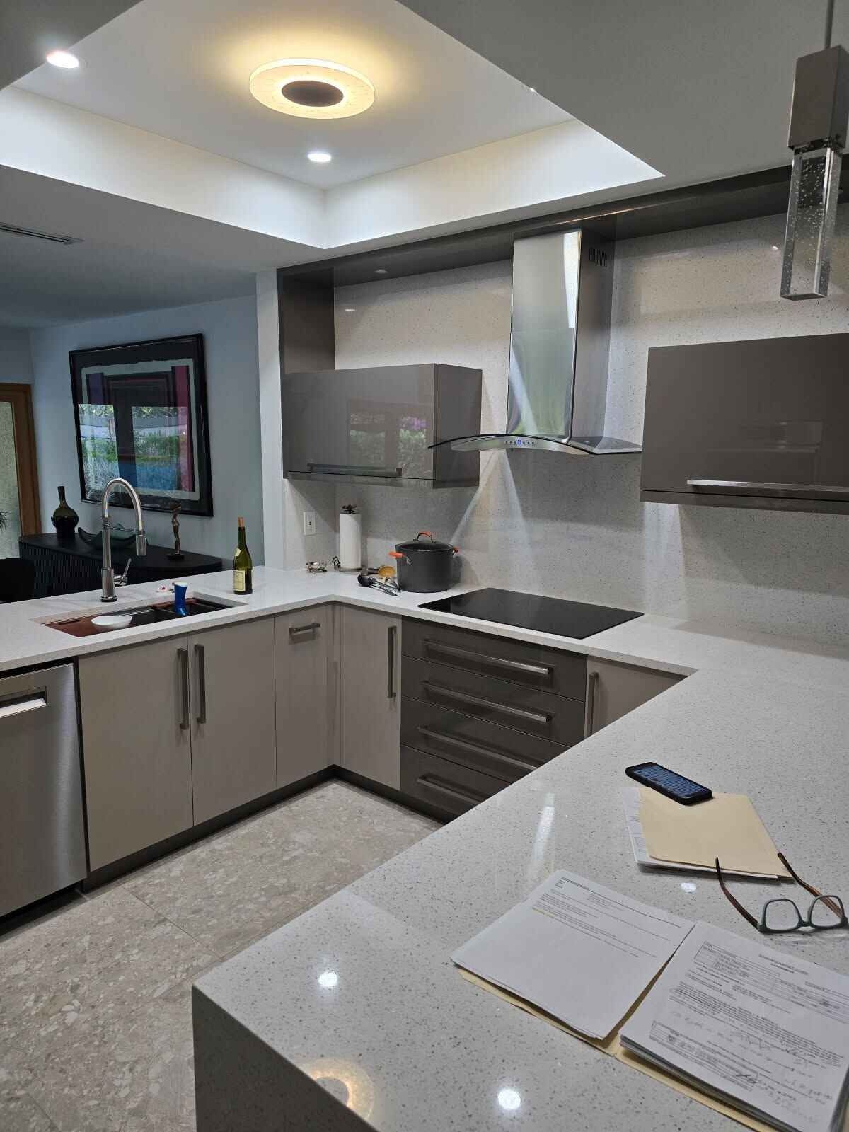 Modern kitchen with gray cabinets, stainless steel appliances, white countertops, and a sink by a window.