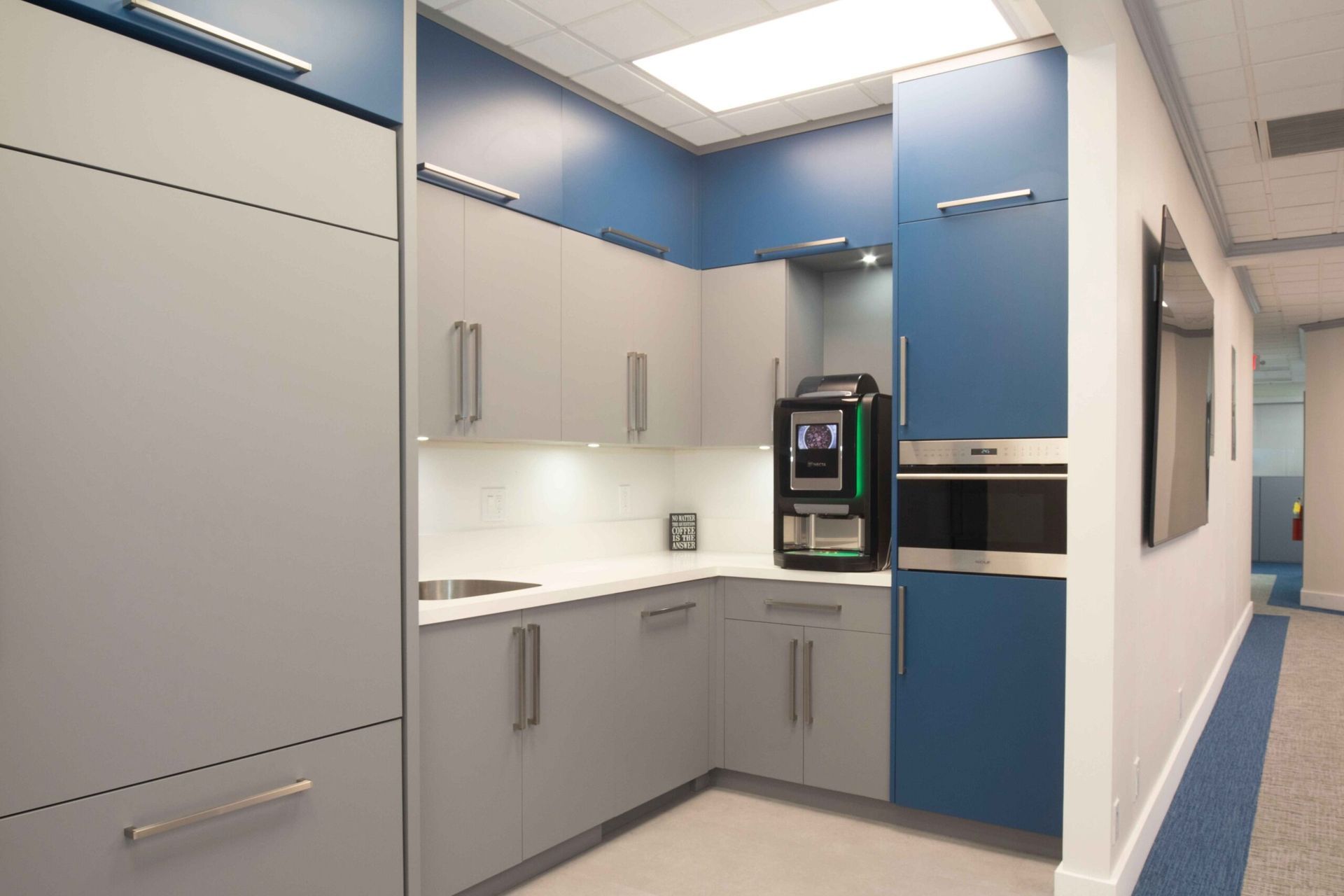 Modern office break room with gray and blue cabinets and a coffee machine