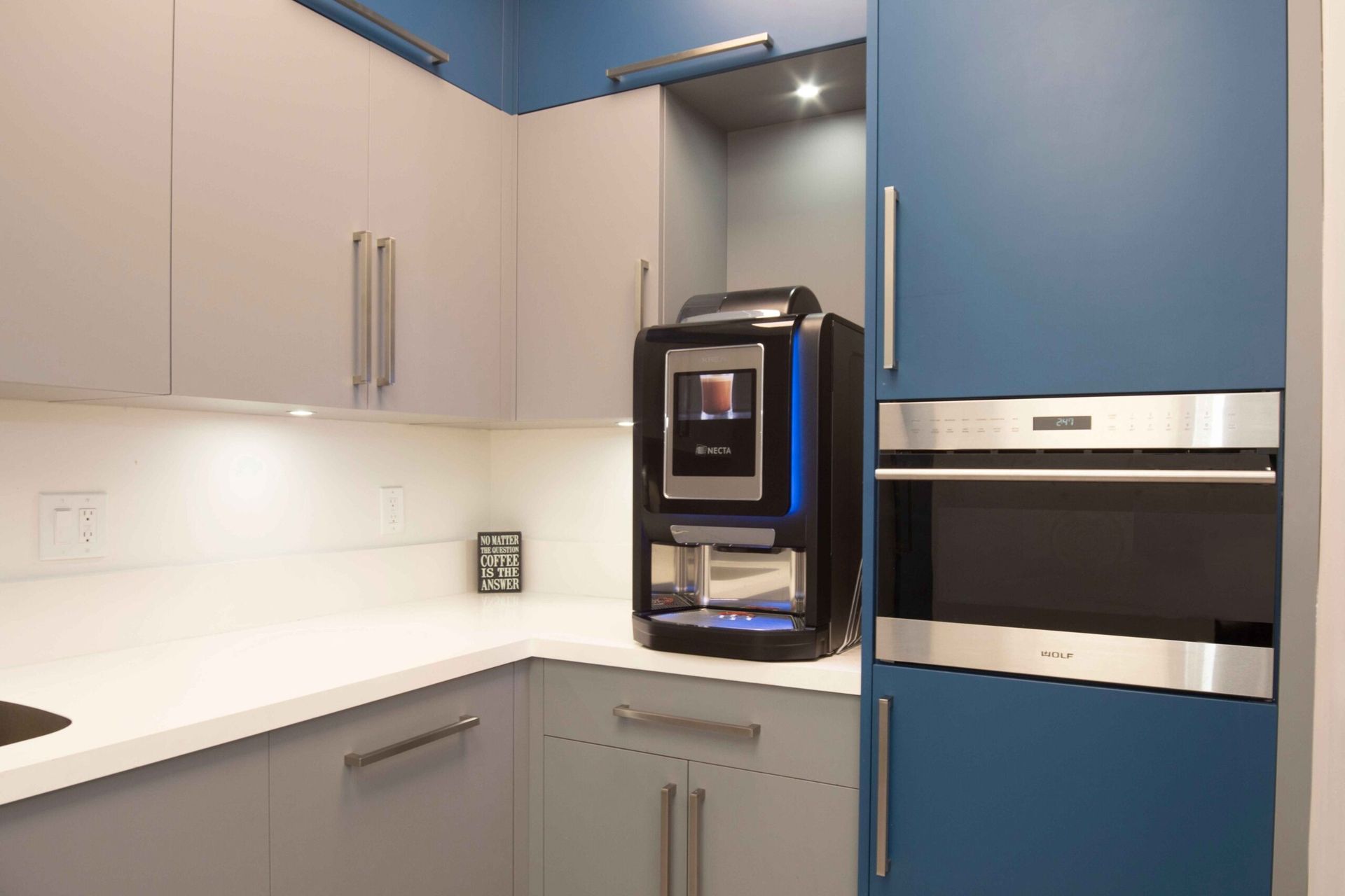 Modern kitchen with white and blue cabinets and a stainless steel coffee machine built into the wall.
