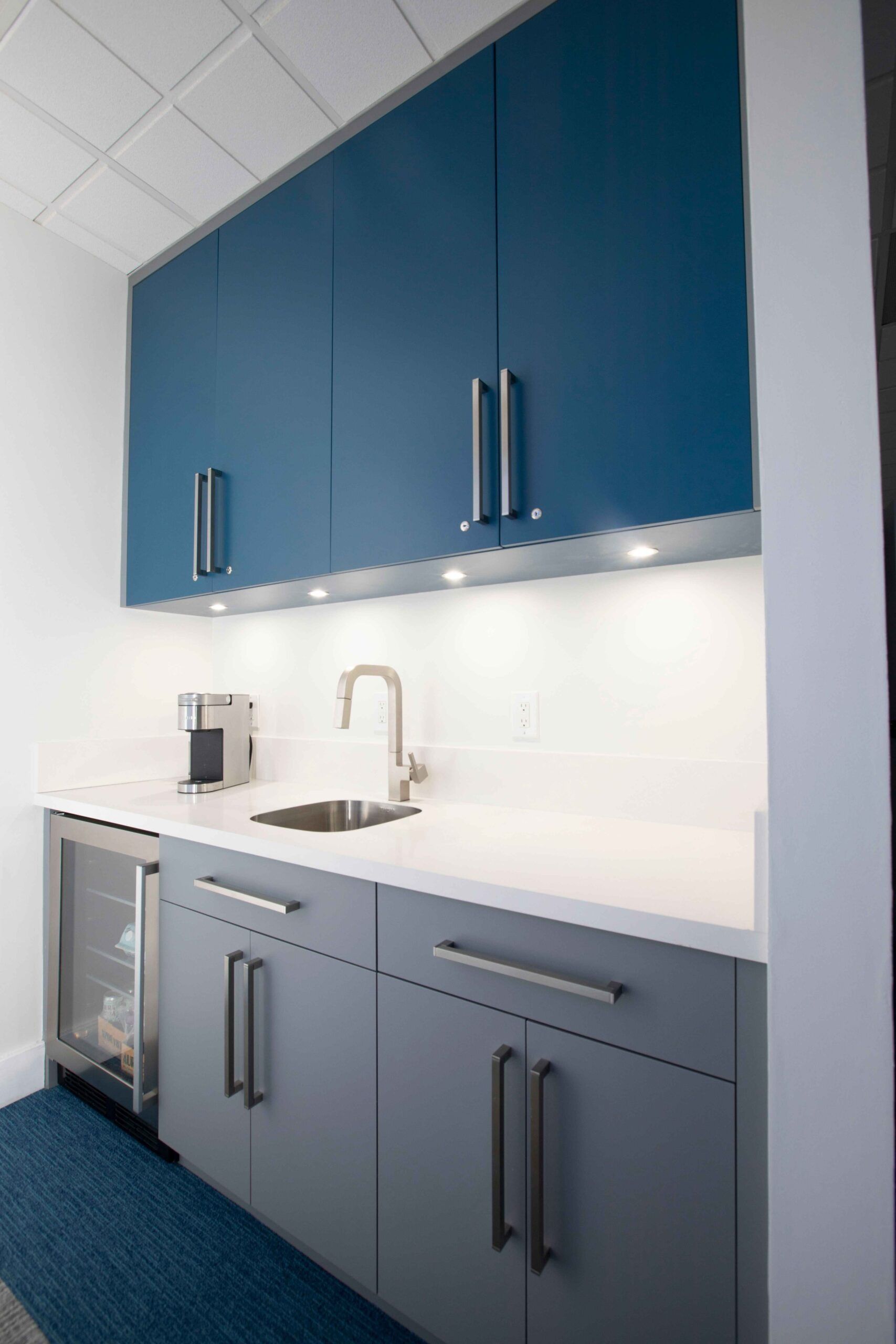 Blue office kitchenette with cabinets, sink, and countertop against a white wall